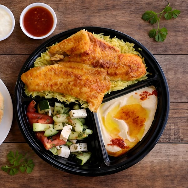 Fried fish fillets with yellow rice, cucumber and tomato salad, hummus, and sauces in a black to-go container.