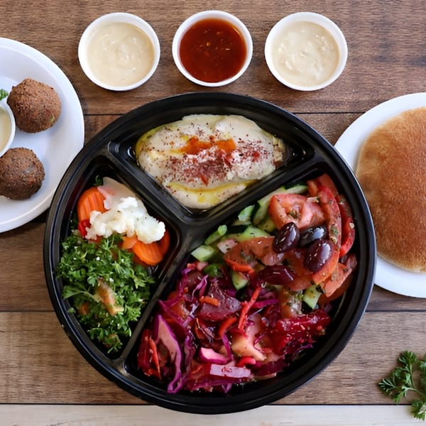 Overhead view of a Mediterranean platter with hummus, falafel, salads, and pita bread on a wooden table.