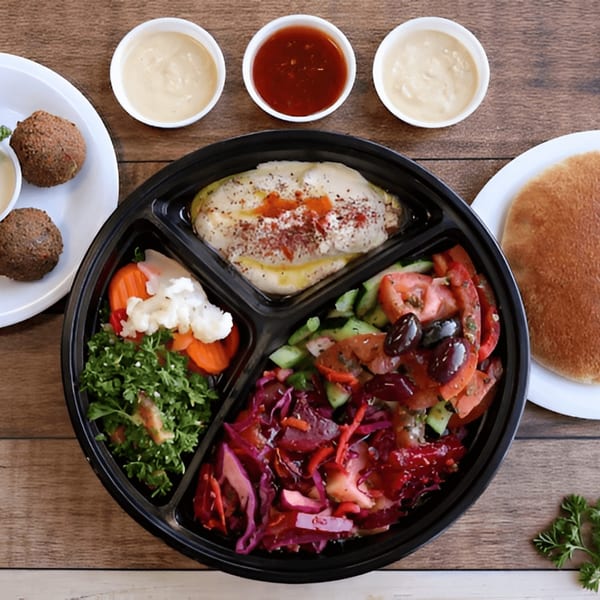 Chicken and salad platter with falafel, pita bread, and three dipping sauces on a wooden table.