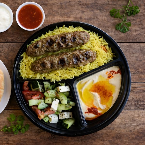 Grilled kofta kebabs on yellow rice, with a side salad and hummus, in a black divided plate.
