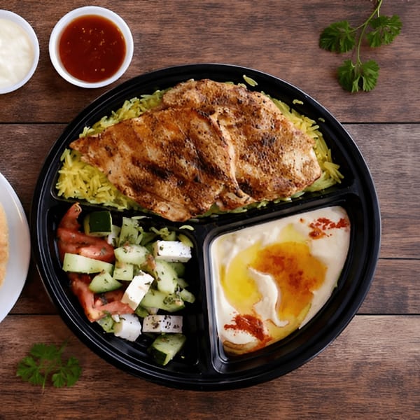Grilled chicken, yellow rice, salad, and hummus in a black segmented plate on a wooden table.